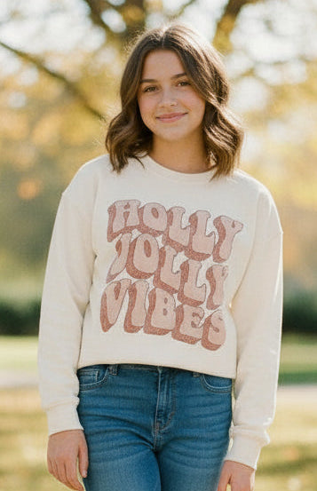 A beige long sleeve cotton jersey t-shirt with the text 'HOLY JOLLY VIBES' printed in a festive pattern.