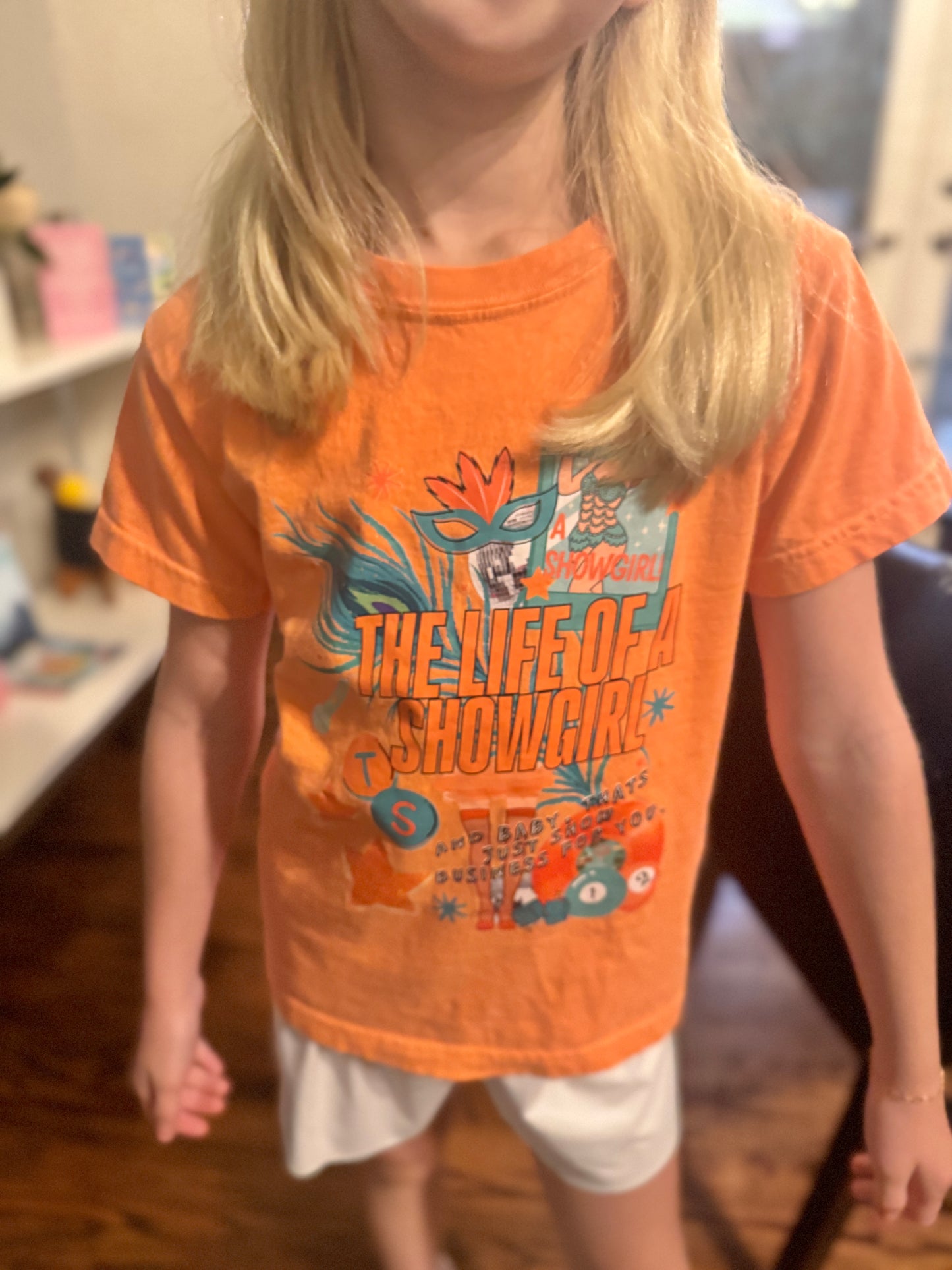 Child wearing an orange t-shirt with taylor swift life of a showgirl graphic design and text