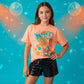 Orange t-shirt with 'The Life of a Showgirl' graphic design on a pink patterned surface.